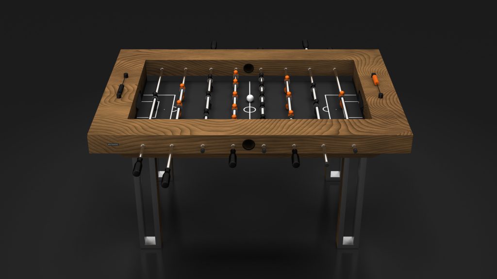 The Executive Foosball Table stands against a black background, featuring a luxury dark metal frame. Metal rods with black handles hold orange and black player figures, while the foosball ball is prominently centered on the field.