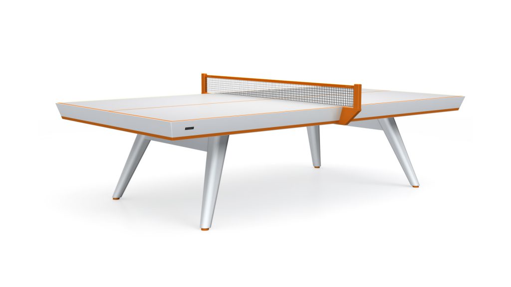 The Hamptons Ping Pong Table is a luxury piece with a sleek design, featuring a white surface, orange accents, and a black net. It evokes the elegance of the Hamptons and stands on four angled slender legs.