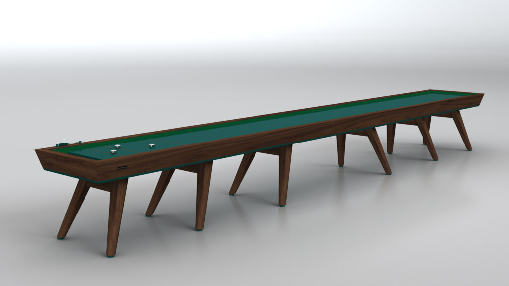 The Hamptons Shuffleboard Table, featuring a dark wood frame, green playing surface, and angled wooden legs, stands on a smooth, light-colored floor in a minimalist room.