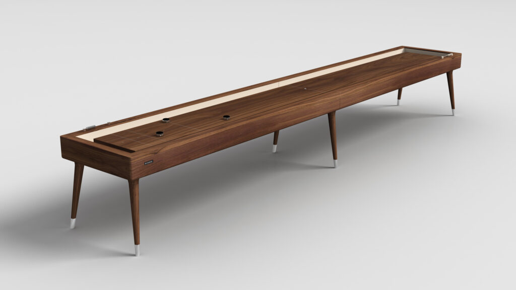 The Hamptons Shuffleboard Table features sleek, tapered legs and a smooth wooden playing surface with pucks on top, all set against a plain white background.