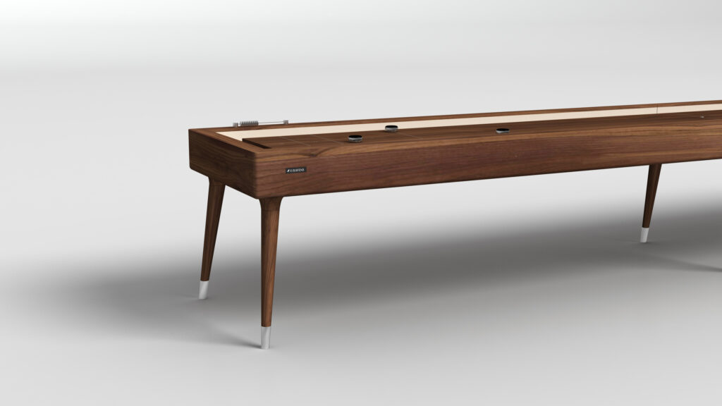 The Hamptons Shuffleboard Table features a wooden finish and sleek, angled legs. Set against a white background, the modern playing surface displays three visible pucks.