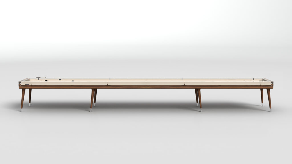 The Hamptons Shuffleboard Table features a long, modern design with a light wood playing surface, slim wooden legs, and clear protective sides, set against a plain white background.