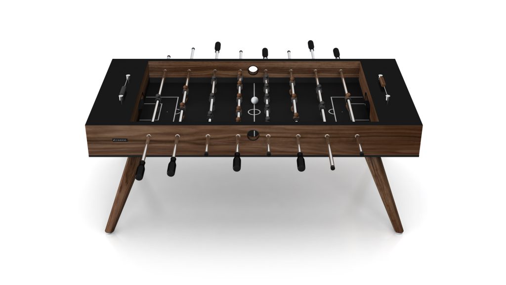 The Hamptons Foosball Table boasts a luxurious design with a black surface, elegant wooden legs, metal rods, and handles. It showcases a white ball centered on a plain white background.