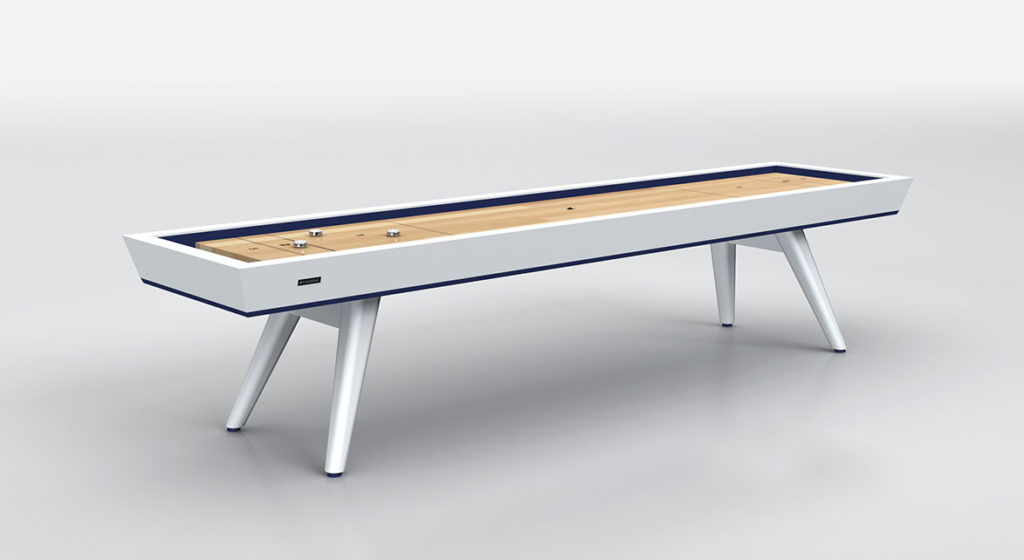 The Hamptons Shuffleboard Table features a sleek design with white legs on a light gray surface, offering an elegant wooden playing area with visible pucks for refined entertainment.