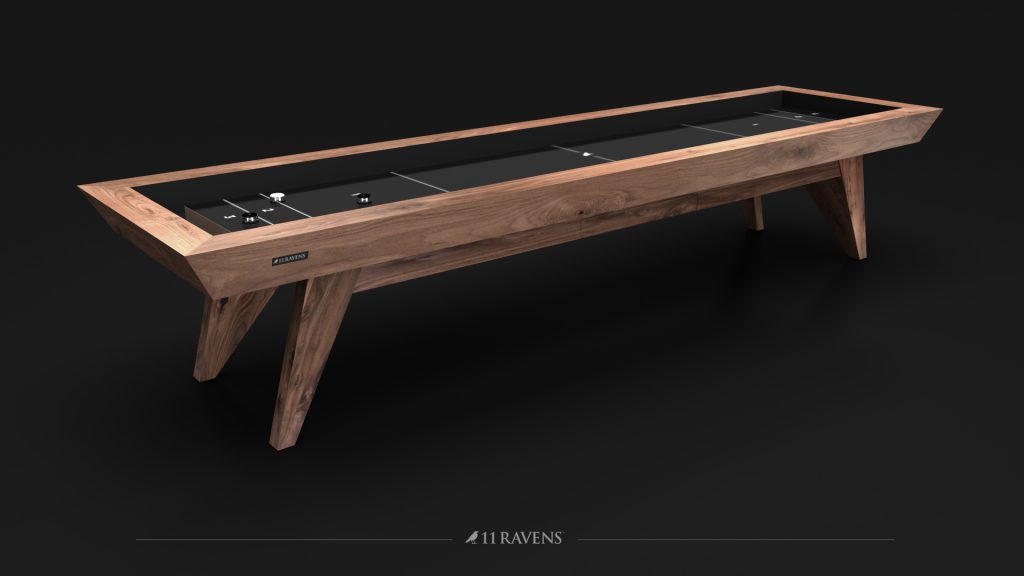 A sleek Trigon Shuffleboard Table with a wooden frame, black surface, and distinctive triangular legs, elegantly displaying the 11 Ravens logo on its side.