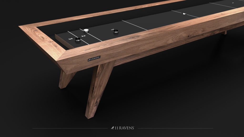 A sleek Trigon Shuffleboard Table by 11 Ravens features a wooden frame and black playing surface with minimalist design, elegantly displaying the 11 Ravens logo on the side against a dark backdrop.