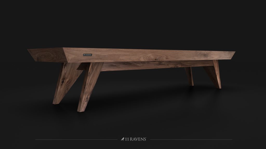 A luxury contemporary wooden table with a dark finish, V-shaped legs, and a rectangular top is set against a black backdrop. Reminiscent of the Trigon Shuffleboard Table by 11 RAVENS, its sleek design includes the brands logo subtly visible at the bottom.