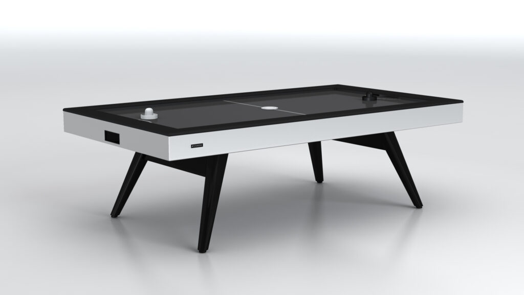 The Hamptons Air Hockey Table features a sleek white and black design with black angled legs and minimalistic details, showcased in a bright studio setting.