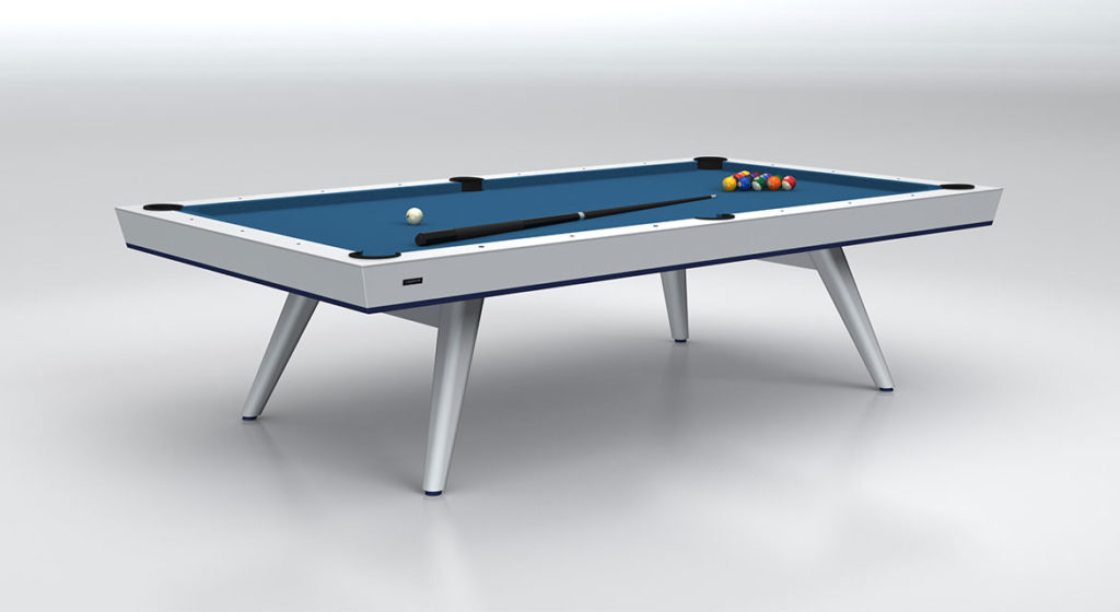 The Hamptons Pool Table is a luxurious piece with a sleek design and blue felt top, featuring six pockets and four slim angled legs. It includes a set of pool balls neatly arranged, perfect for an elegant game room with its simple, light-colored backdrop.