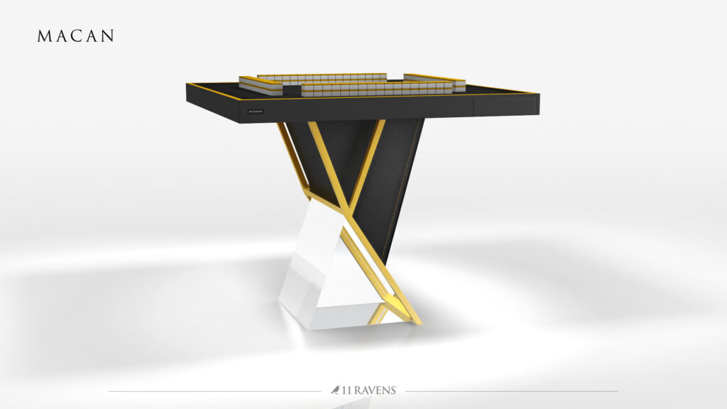 The Macan Mahjong Table features a sleek black and gold top, geometric angles, and a distinctive V-shaped gold and white base. Modern and luxurious, this statement piece has "MACAN" inscribed in the corner.