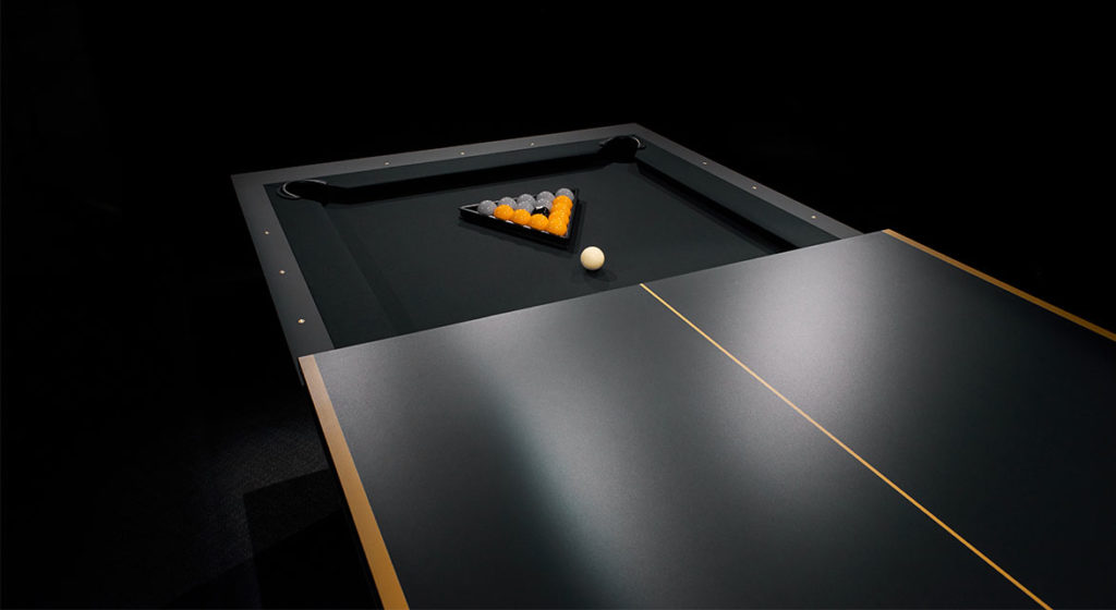 The R11 Stealth Pool Table displays a triangle of billiard balls at one end, with the cue ball ready for the break. It boasts a sleek, modern design with a dark green surface set against an elegant dark background.