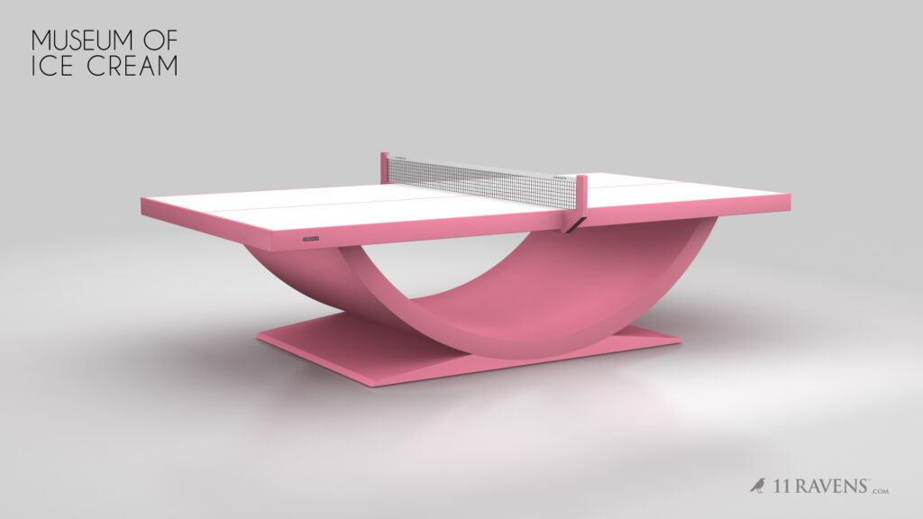 A modern pink Theseus Ping Pong Table with a curved base is showcased in a minimalist space, labeled Museum of Ice Cream in the corner and displaying the 11 Ravens logo at the bottom right.