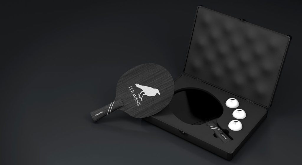 The Ping Pong Case is a sleek black table tennis set symbolizing luxury, featuring a black paddle with the 11 RAVENS stylized raven logo, three white balls, and a padded interior for secure storage.