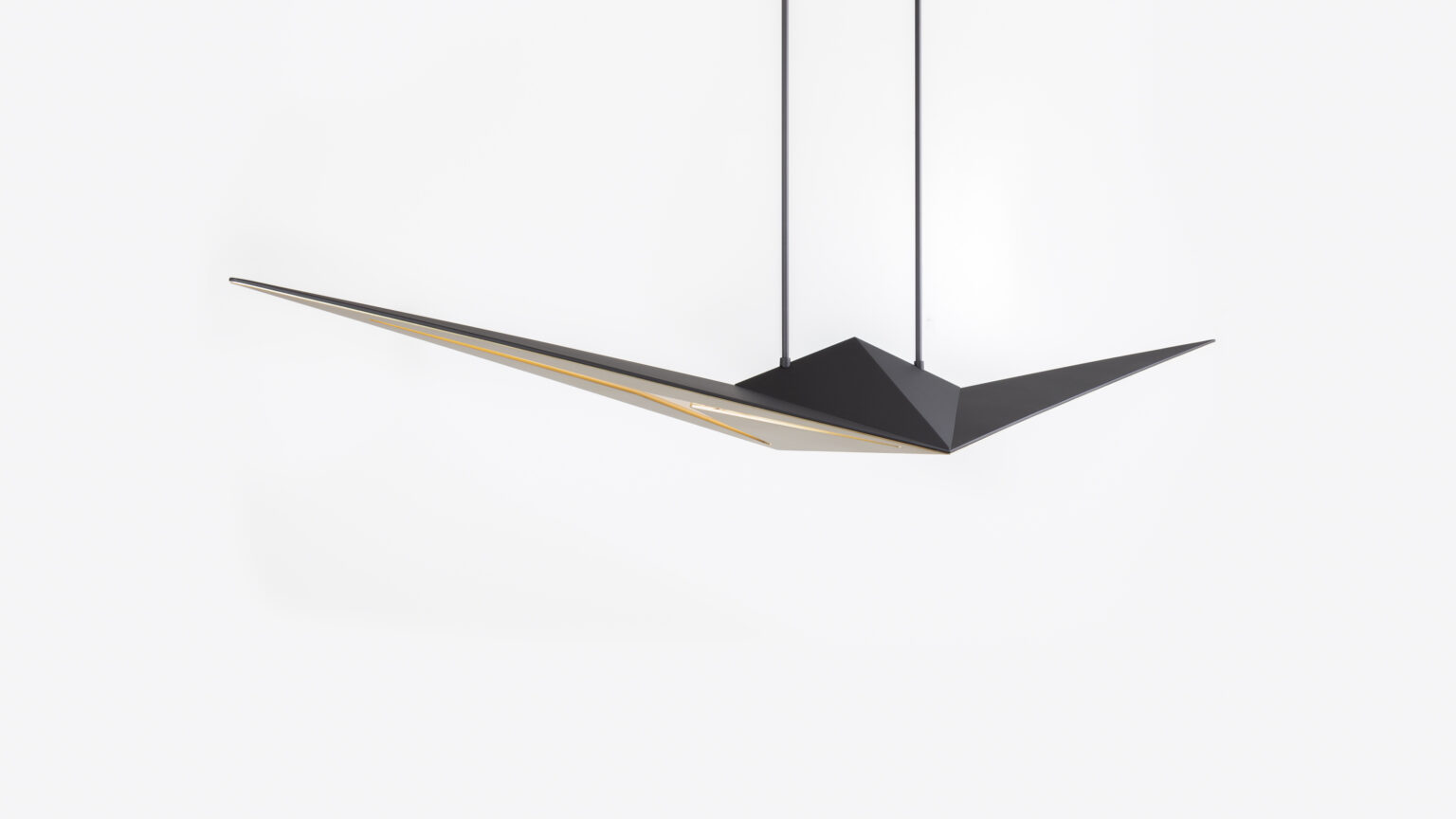 The Áves Pendant Light has a modern, geometric design with sleek angles similar to luxury game tables. It features two long, pointed edges and hangs from two cables against a white background, providing a minimalist and contemporary look.