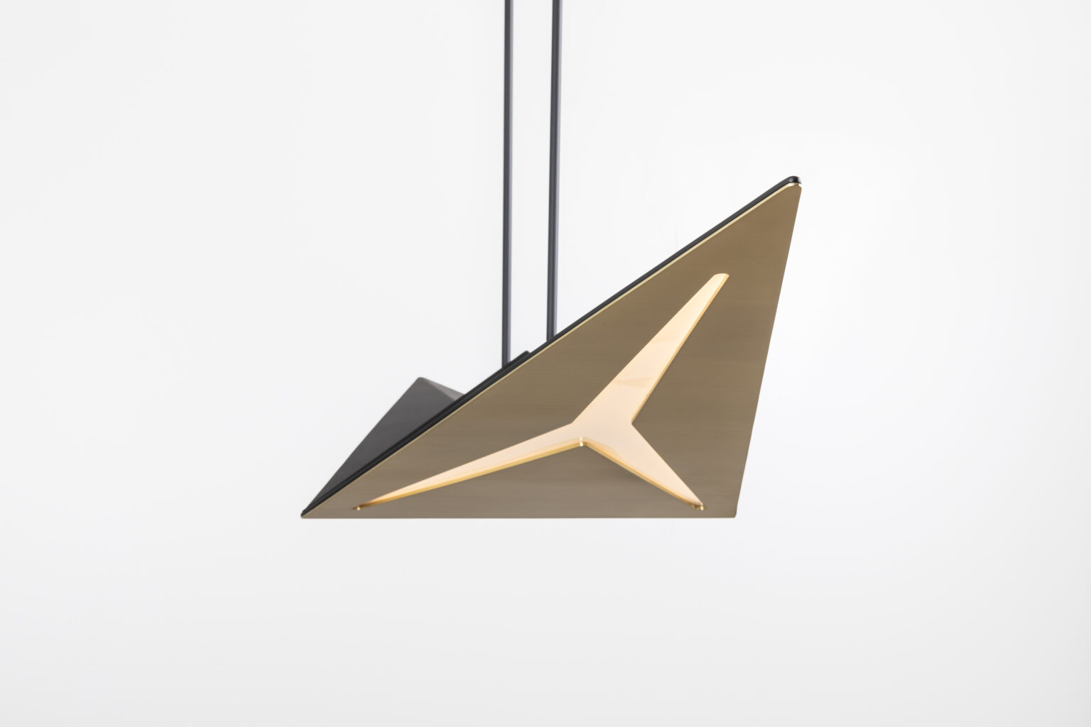 The Áves Pendant Light, with its sleek triangular design and metallic finish, serves as a statement piece in a room adorned with luxury game tables. Its minimalist geometry and illuminated interior stand out against the plain white background.