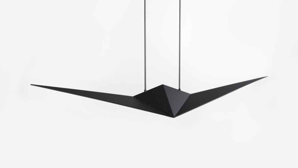 The Áves Pendant Light, featuring a minimalist design like a folded black paper plane, exudes sophistication similar to luxury game tables, suspended by two cords against a plain white background.