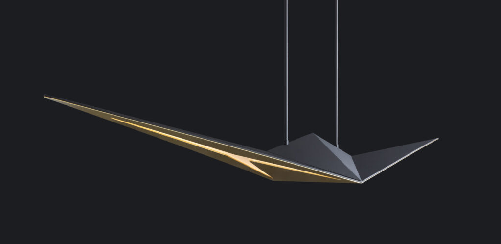 The Áves Pendant Light is a modern, angular fixture with sharp edges and a sleek design, reminiscent of luxury game tables. Suspended by two thin cables, it has a dark exterior with a gold interior, creating an elegant contrast against the black background.