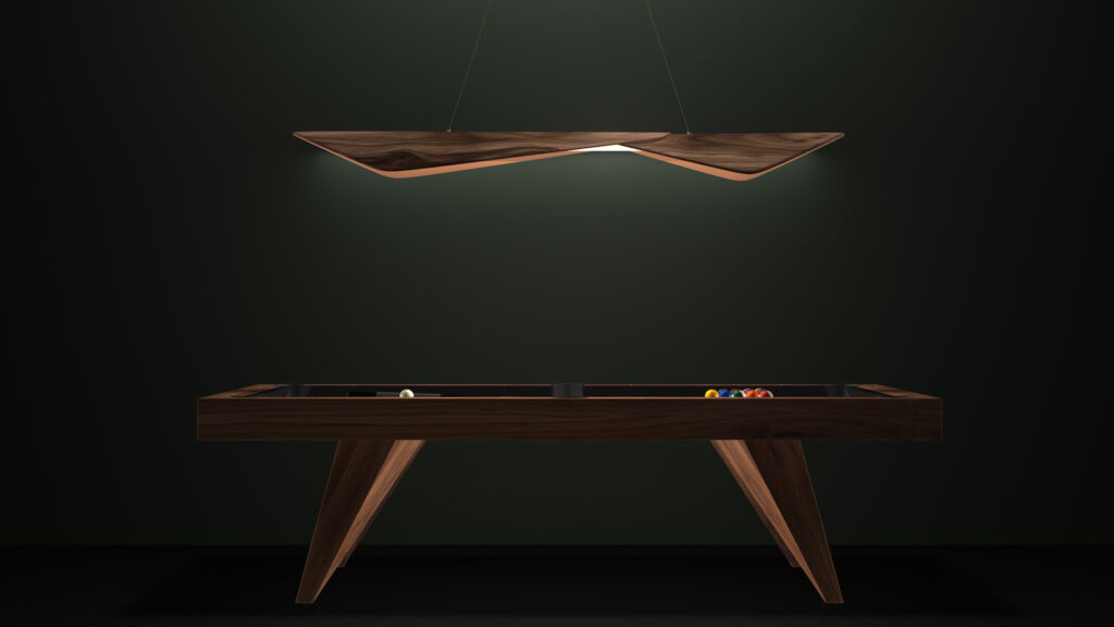 A sleek, modern billiards table with a dark wood finish stands against a dark green wall, epitomizing luxury. Colorful pool balls are neatly arranged on it. Overhead, the Folio Pendant Light with its unique curved design brightly illuminates the scene.