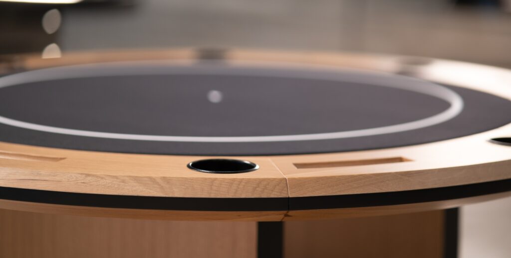 A close-up of the 5 Theseus Round Poker Table - Off The Floor, showcasing its elegant round design with a refined wooden border, dark playing surface, card slots, and cup holder against a softly blurred background.