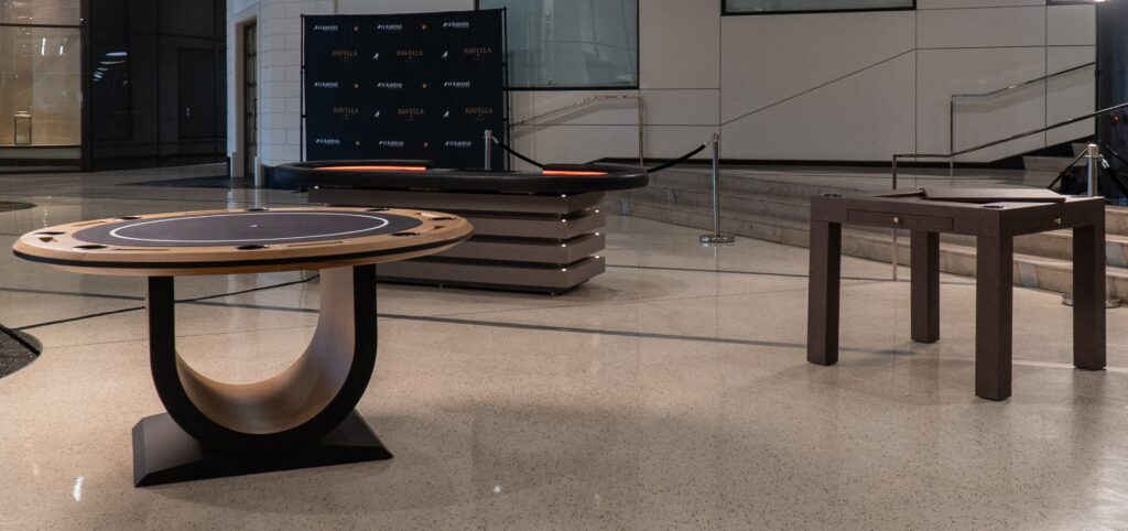 The empty room features three luxury game tables, including a 5 Theseus Round Poker Table with a modern curved wooden base, a rectangular table with a rail, and a minimalist square design. The polished floor enhances elegance, while subtle signs linger in the background.