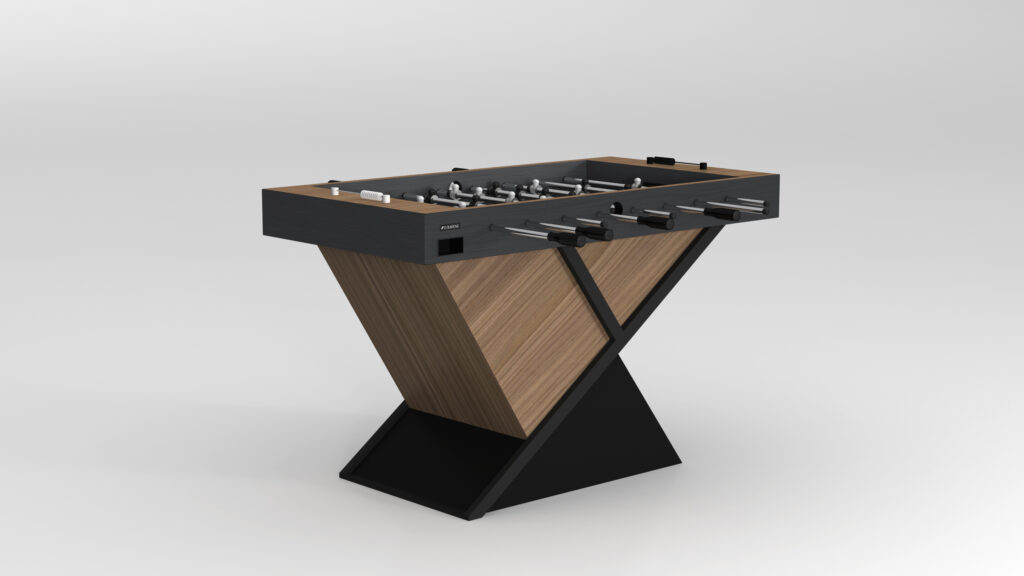The Macan Foosball Table boasts a modern design with a unique V-shaped base and luxurious wood and dark accents. It features metal rods with handles, player figures, and stands out against its plain, light-colored background in the realm of luxury game tables.