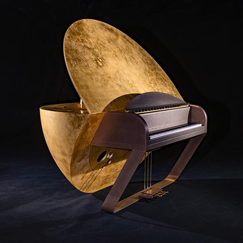 A grand piano with an unconventional design featuring a large, golden, textured, semi-circular structure replacing the traditional lid, set against a dark background.
