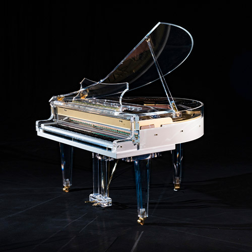 An Edelweiss Pianos transparent grand piano with a raised lid, clear body, and legs, accented with gold fittings, is displayed against a black background.