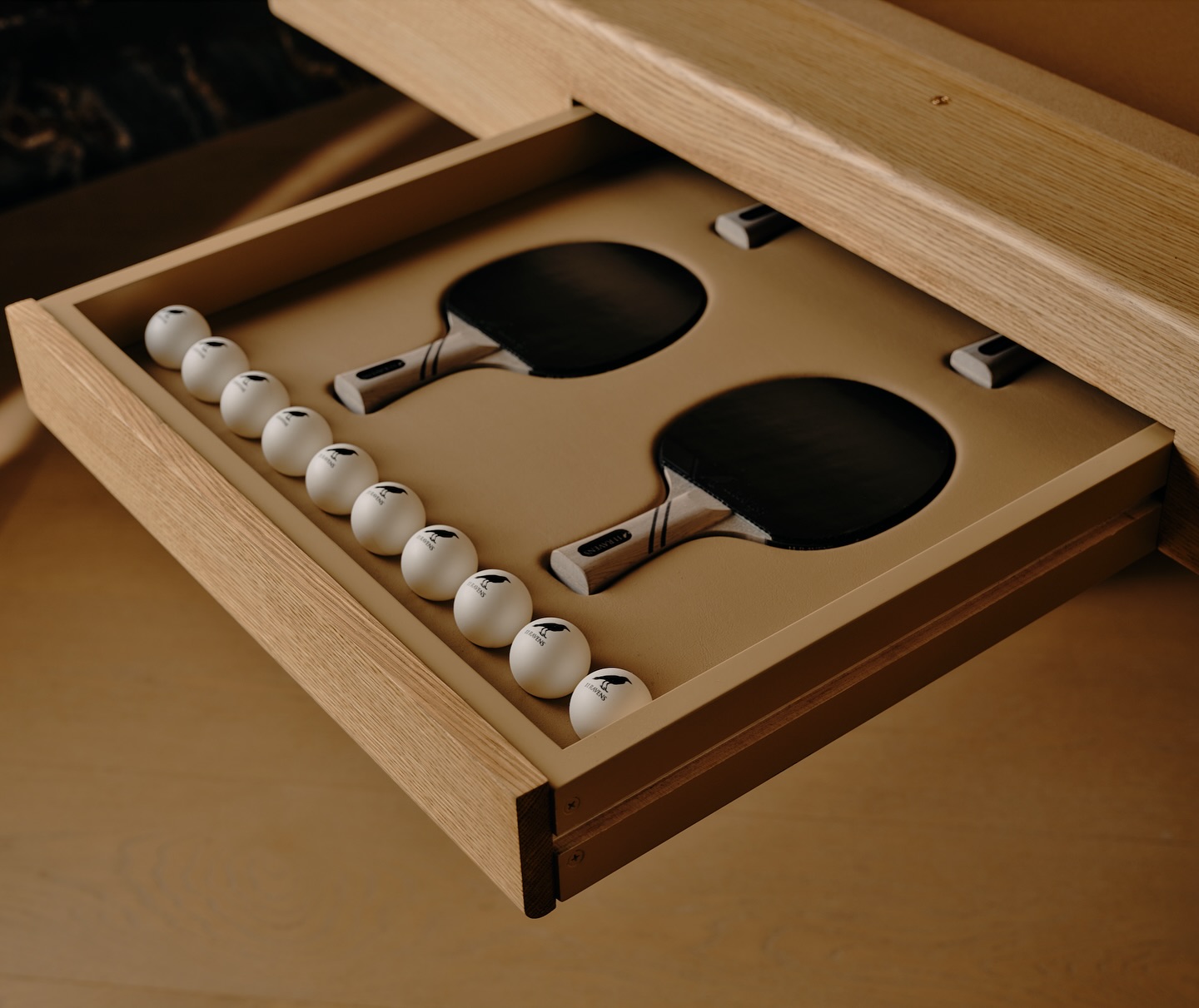 An open wooden drawer contains two table tennis paddles and ten white ping pong balls neatly arranged in a custom beige tray.