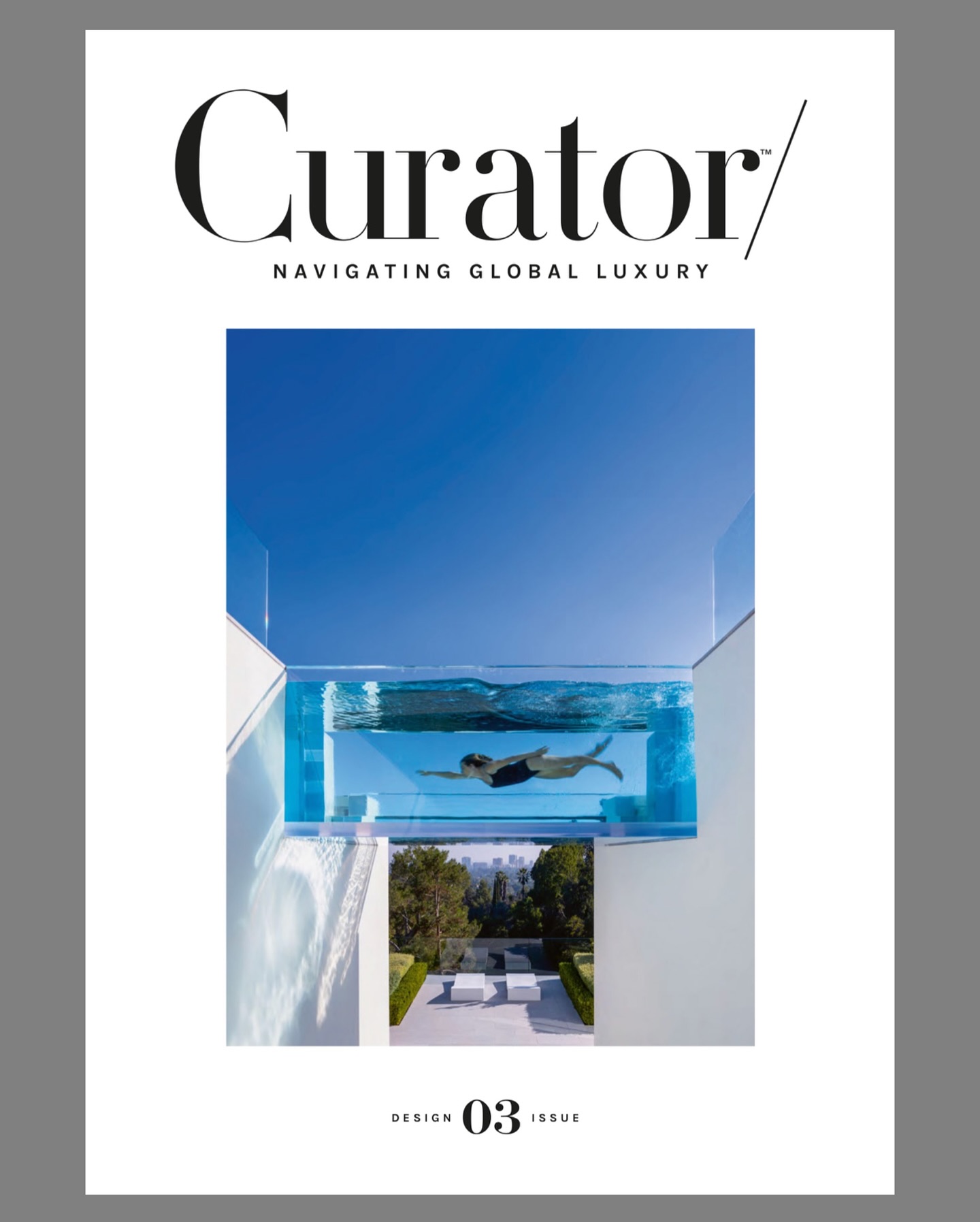 Cover of Curator magazine, featuring a person swimming in a transparent elevated pool with a clear blue sky and modern architecture in the background; text reads Navigating Global Luxury and Design 03 Issue.
