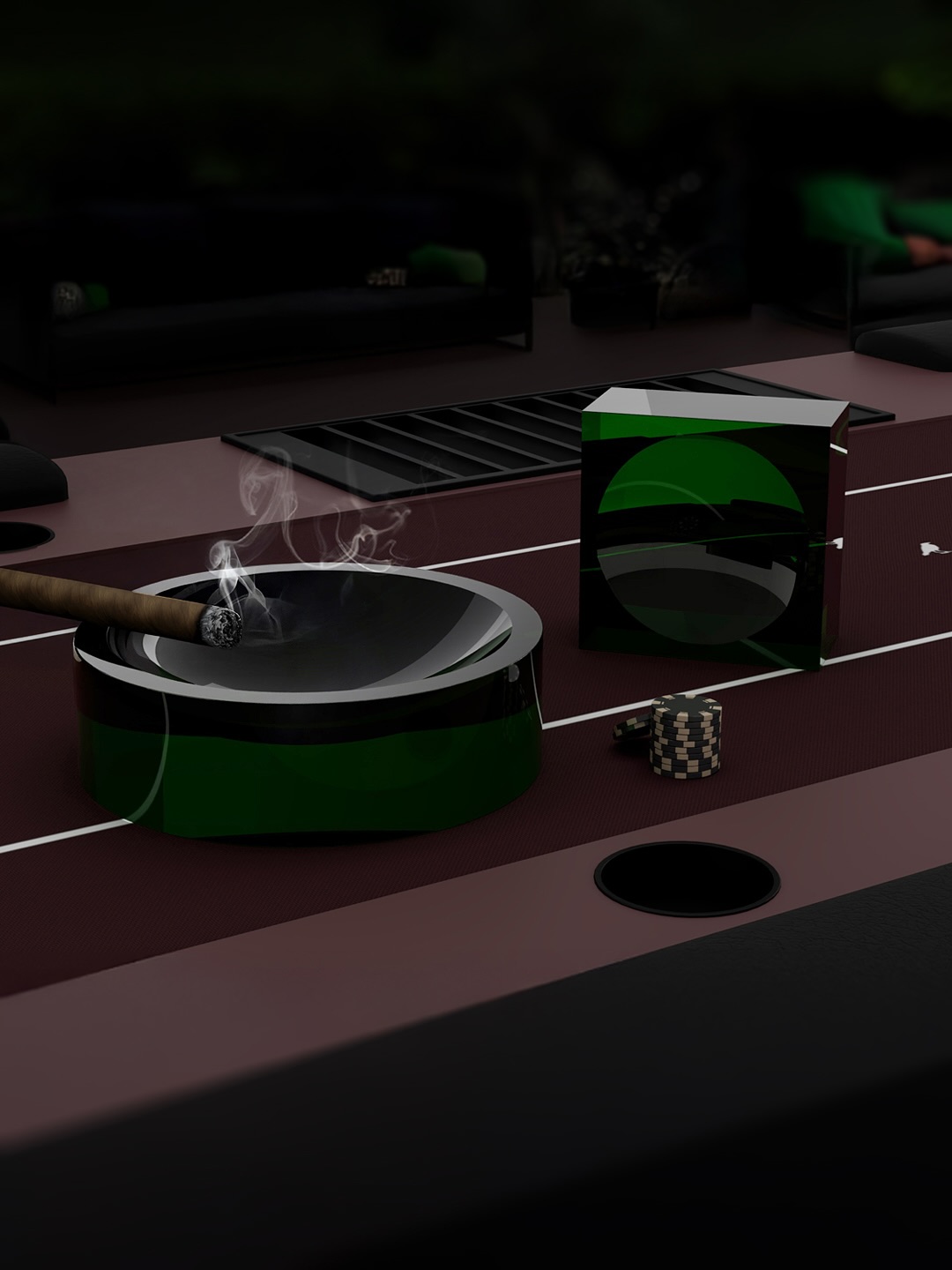 A lit cigar rests in a green glass ashtray on a dark table. Nearby are a green and black cigar box and a small, checkered item. The background is dimly lit with blurred objects and furniture.