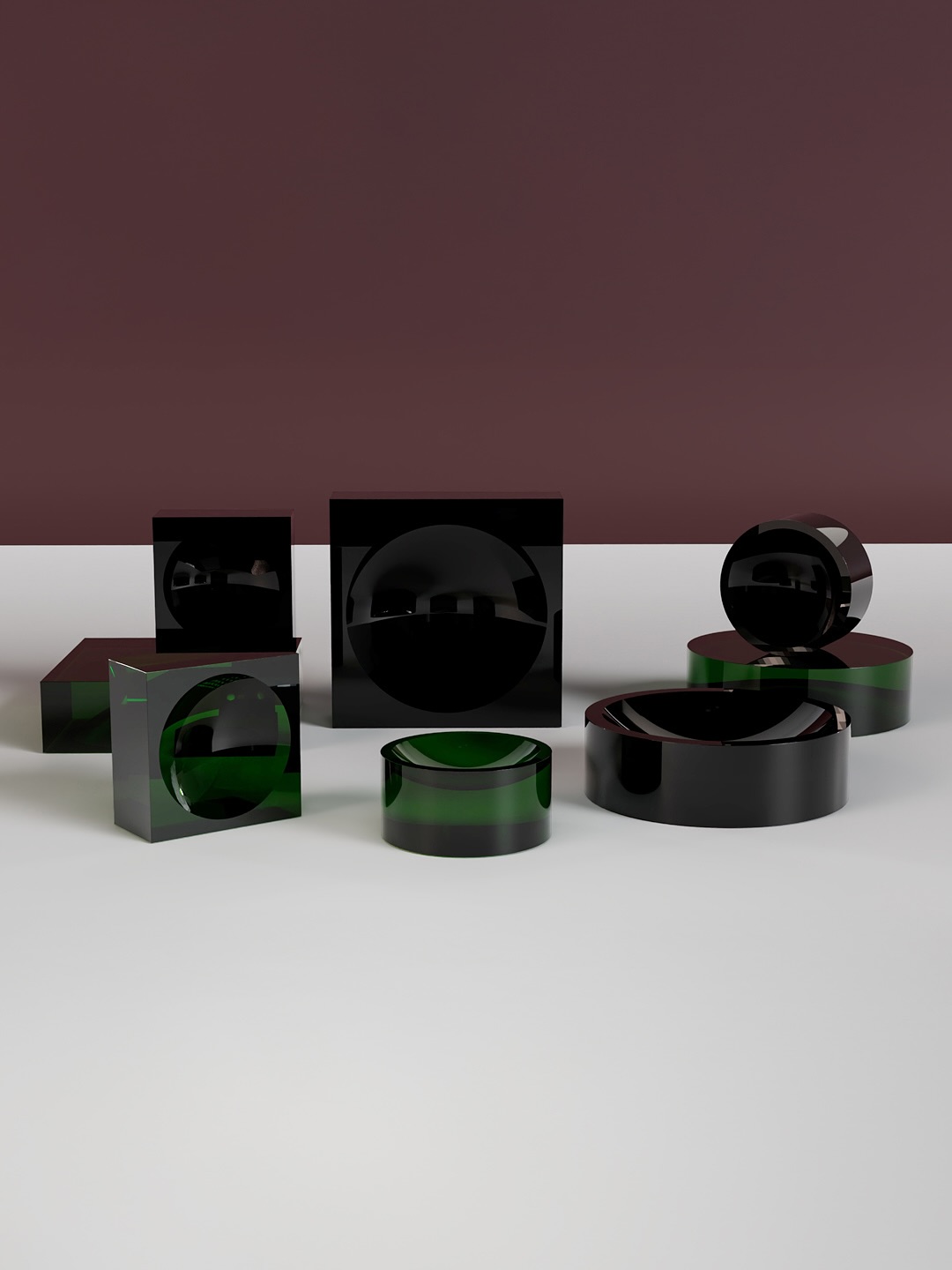 Several glossy, dark green and black geometric shapes—cubes and cylinders—are arranged on a white surface, with a maroon wall as the background. The scene features reflections and subtle lighting.