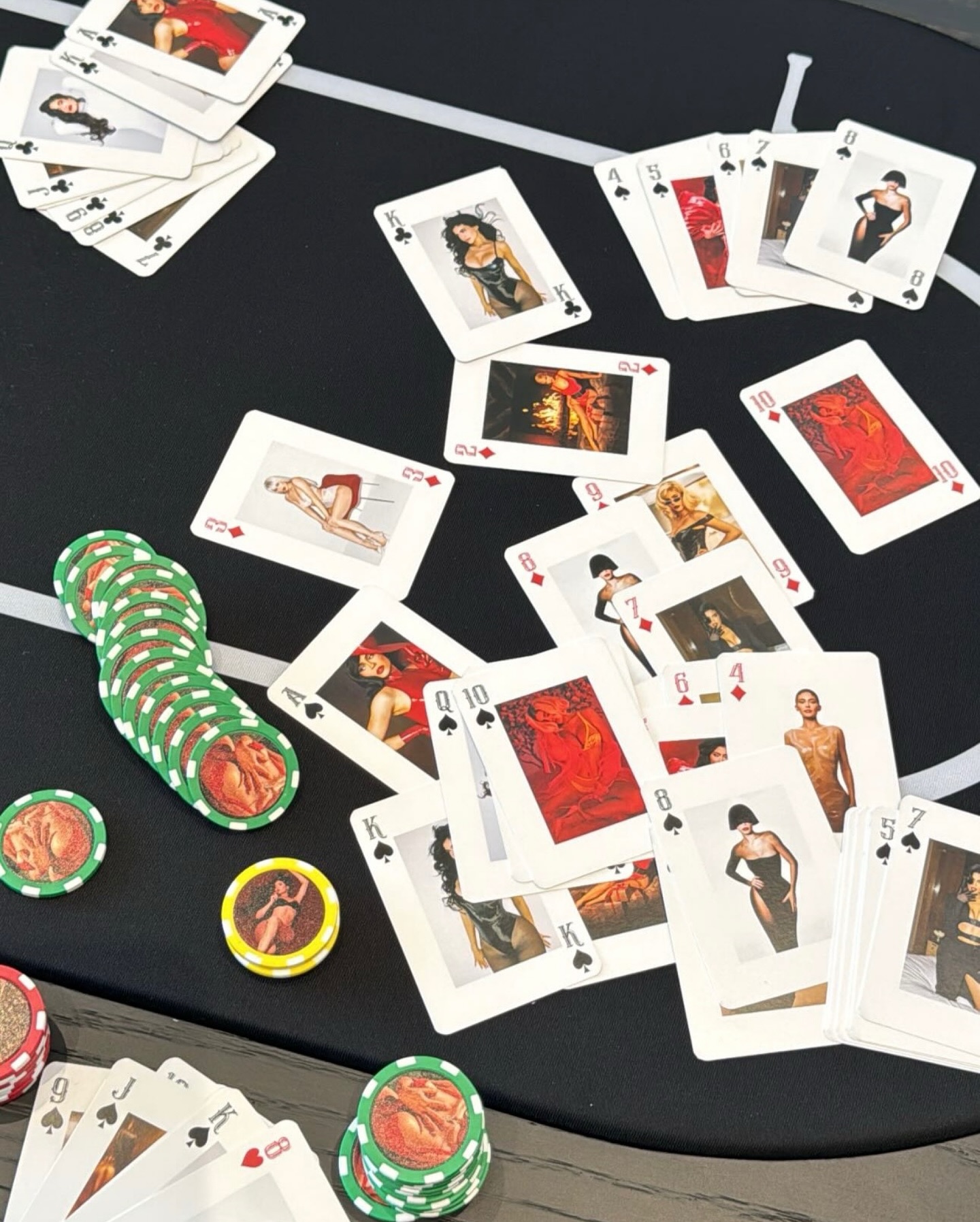 Playing cards with images of women in various poses are scattered on a blackjack table, alongside stacks of green and yellow poker chips.