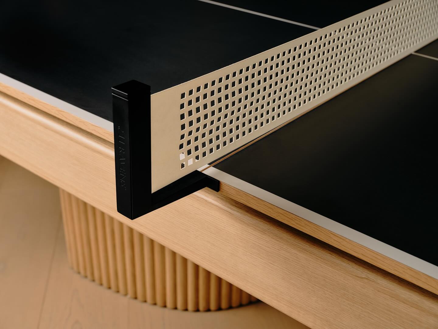 Close-up of a modern convertible game table: this ping pong table features a beige wooden base, black playing surface, and perforated white net with black clamp—perfect for any interior designer seeking a sleek, multifunctional piece.