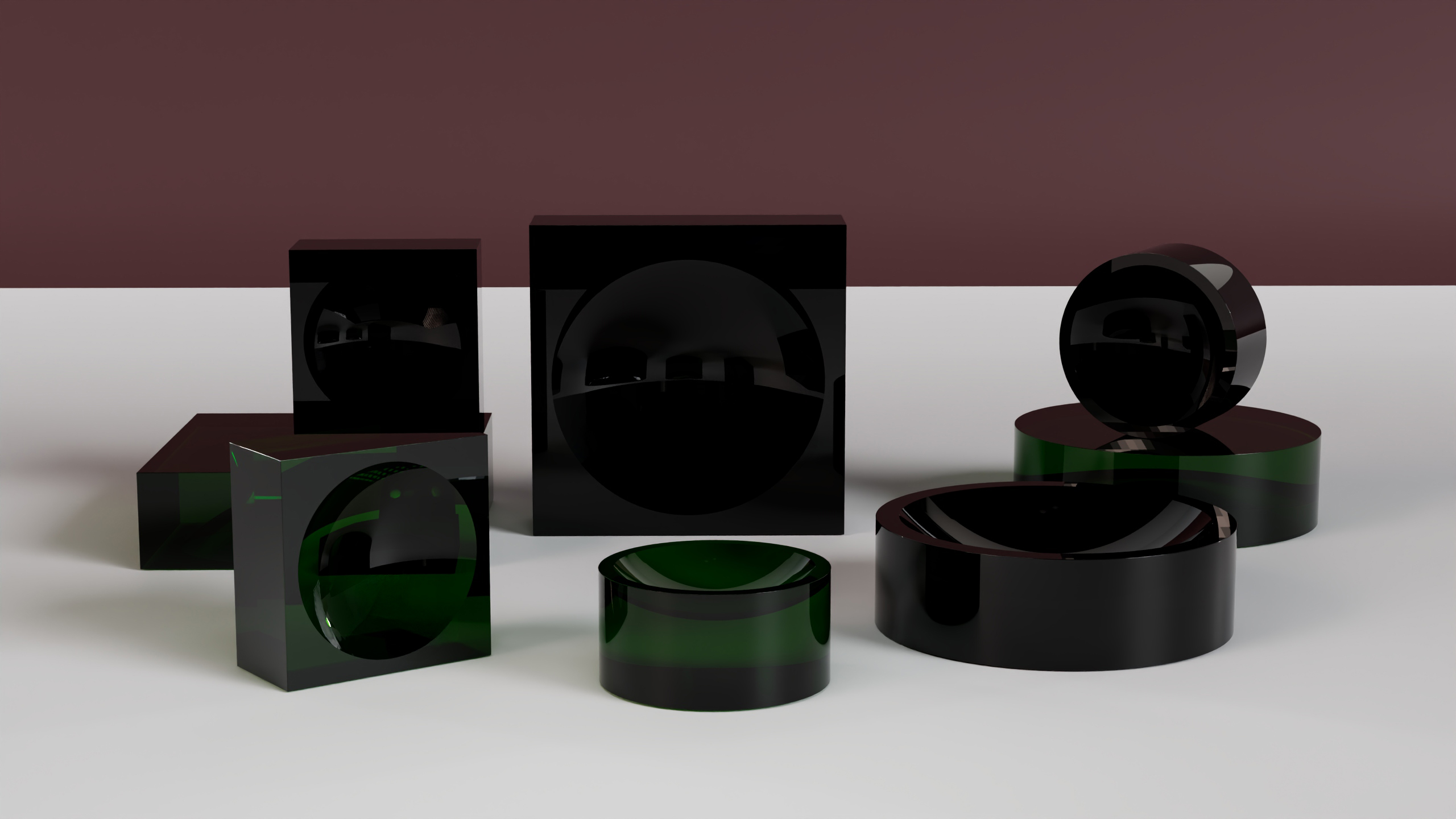 A group of glossy black and green geometric shapes, including cubes, cylinders, and spheres, are arranged on a white surface with a brown background. The objects cast subtle reflections and shadows.