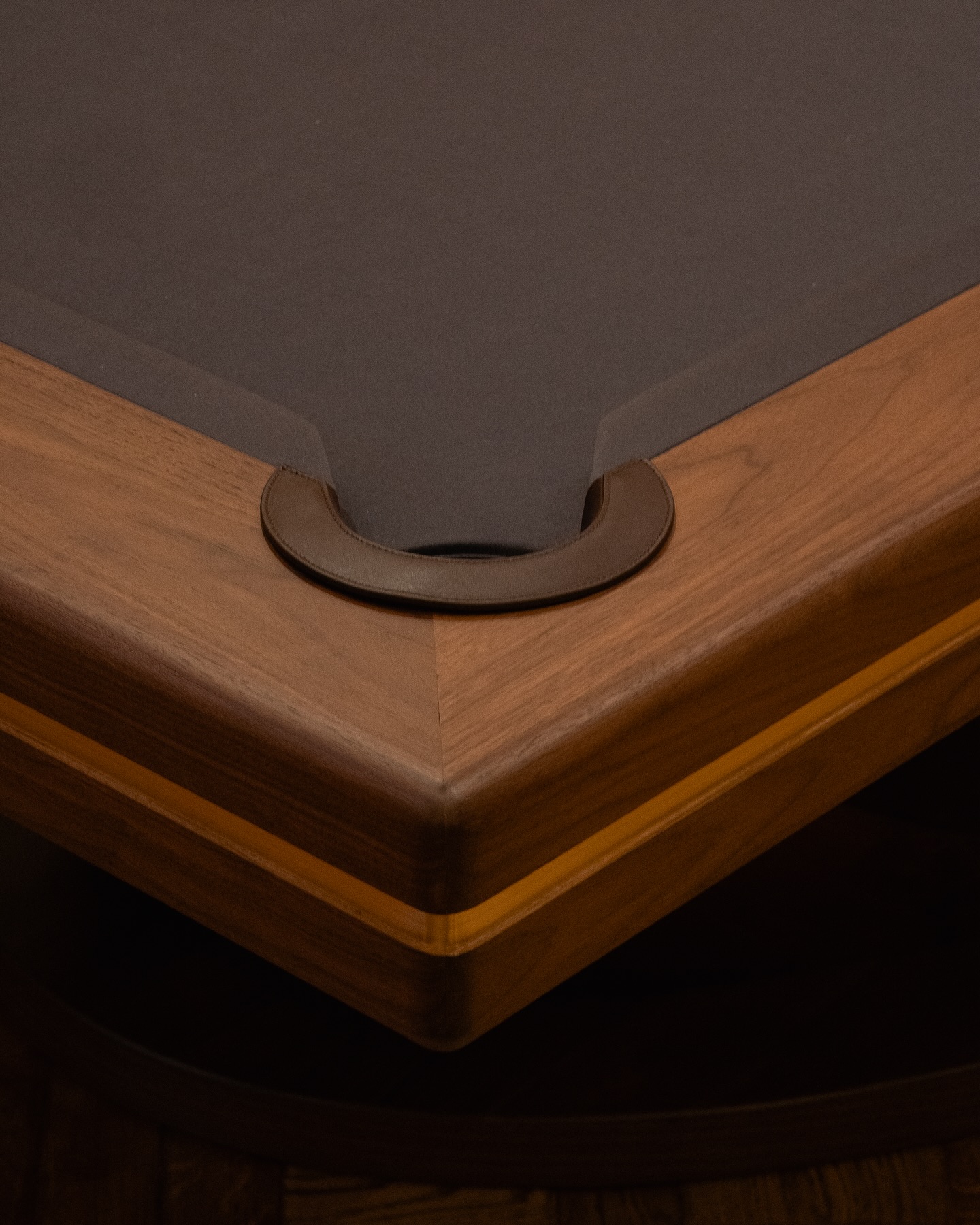 Close-up of the corner pocket of a wooden pool table with a dark playing surface.