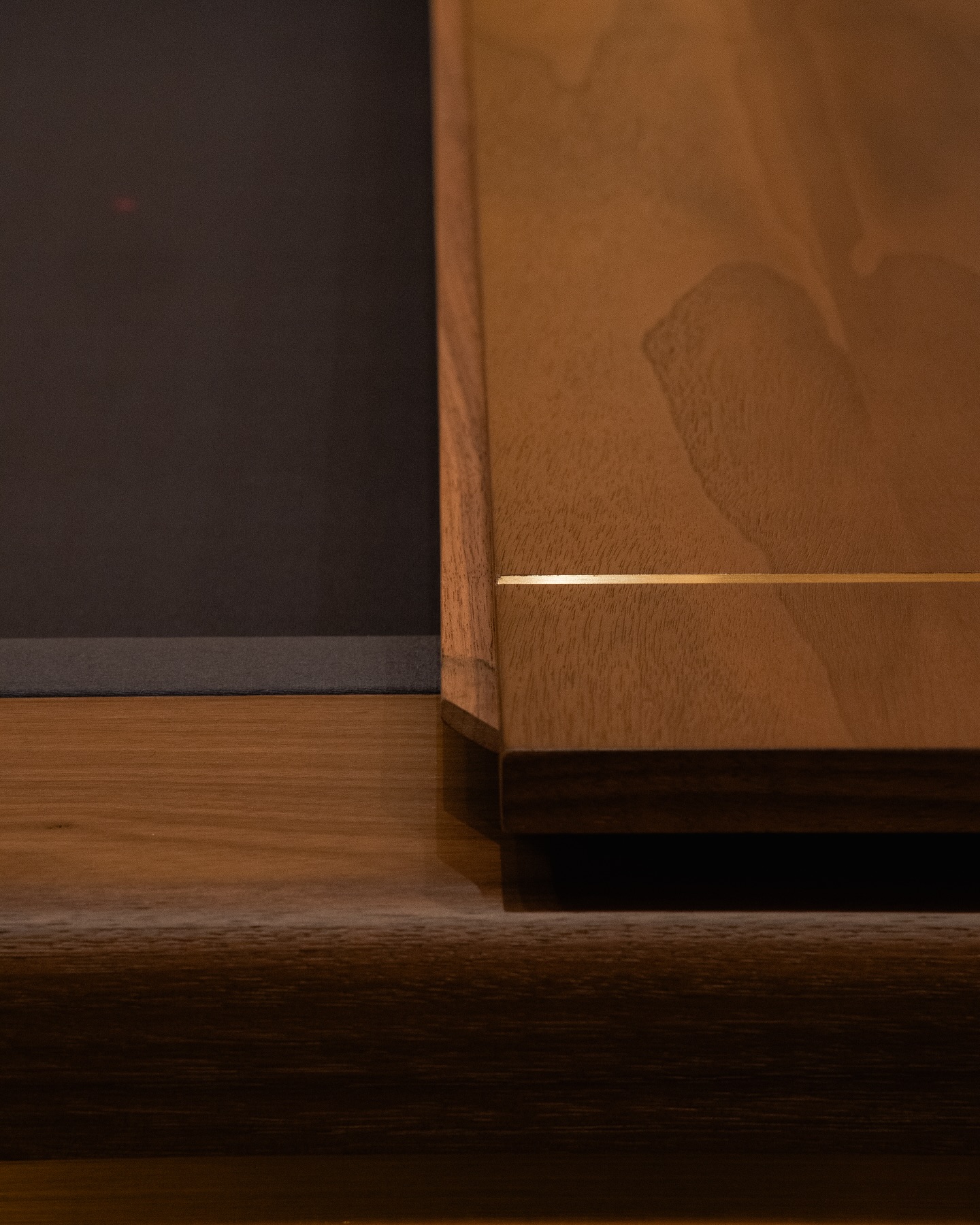 A close-up of a wooden table with a polished surface and a subtle golden line detail next to a dark-colored placemat or panel on the left side.