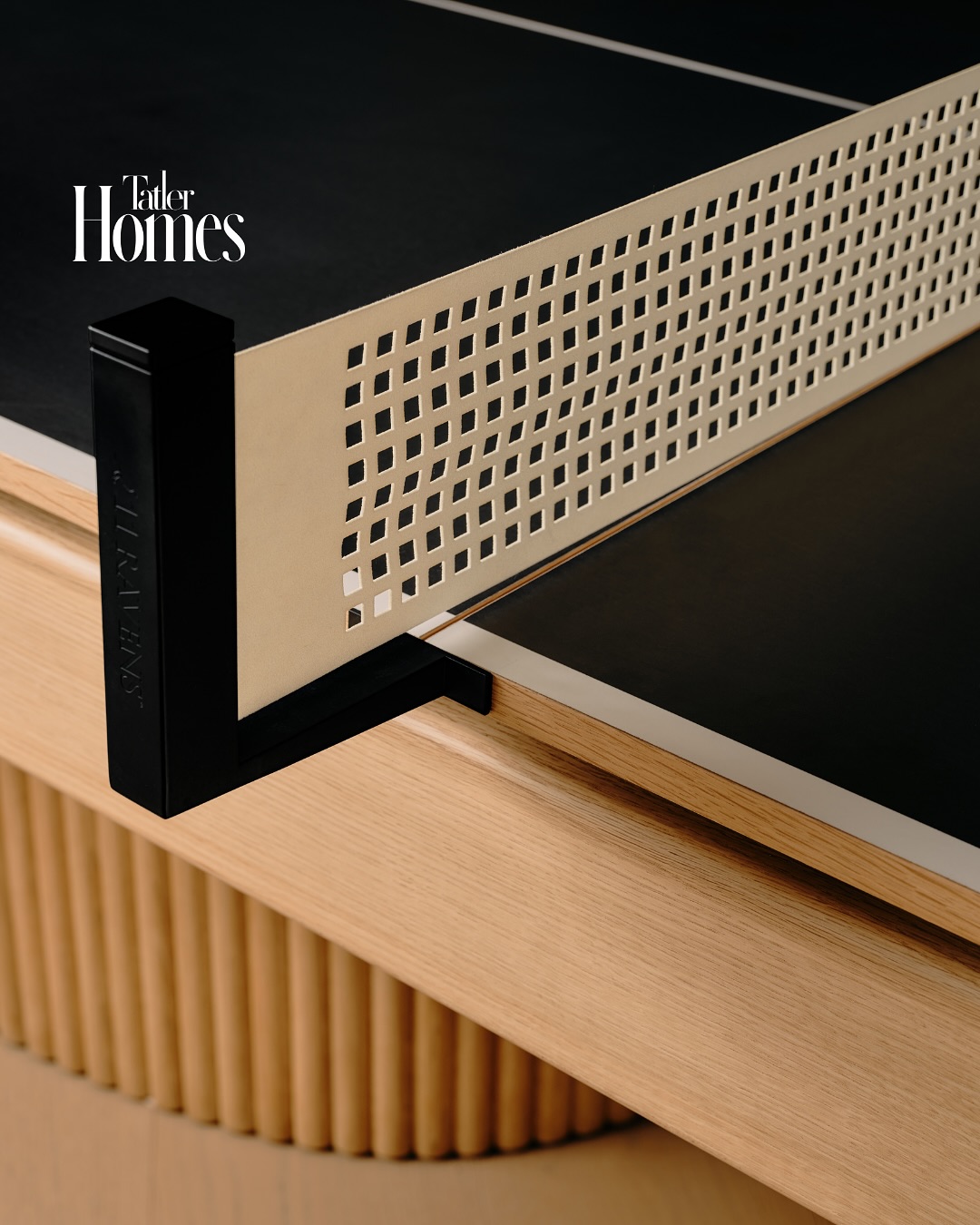 A close-up of a modern ping pong table with a black and beige color scheme, a grid-patterned net, and a light wood base—designed to impress any interior designer. The Tatler Homes logo appears in the top left corner.