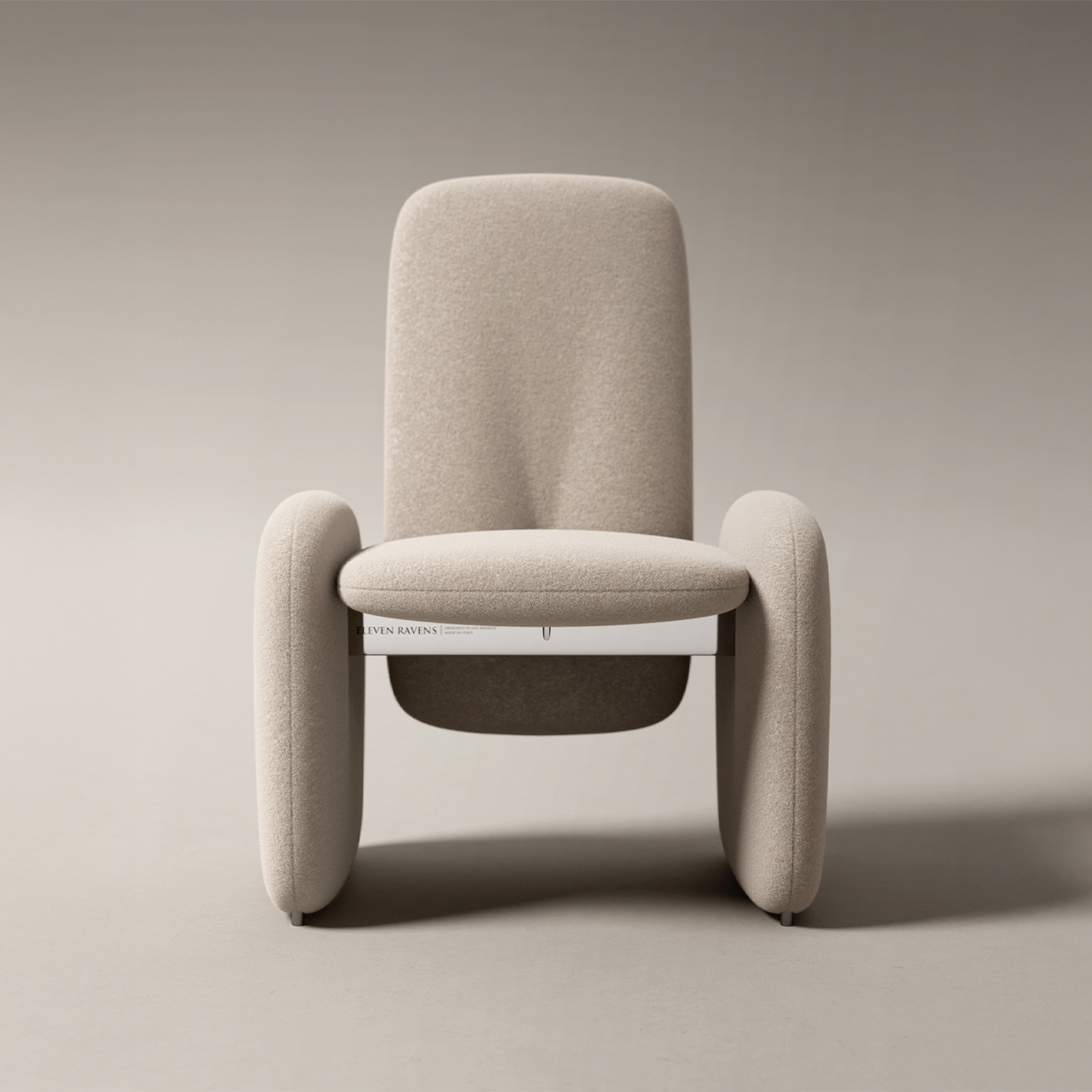 A modern, minimalist armchair with soft, rounded edges and light beige upholstery is shown against a plain, neutral background. A magazine is tucked horizontally beneath the seat—perfect seating for relaxing to Edelweiss Pianos in style.