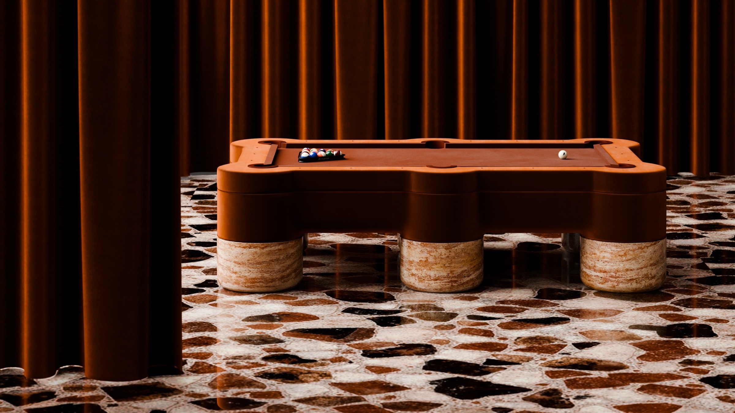 A Marc Ange Pool Table with a brown felt surface and chunky stone legs sits on a mosaic stone floor, complemented by brown curtains in the background for a warm, stylish look.