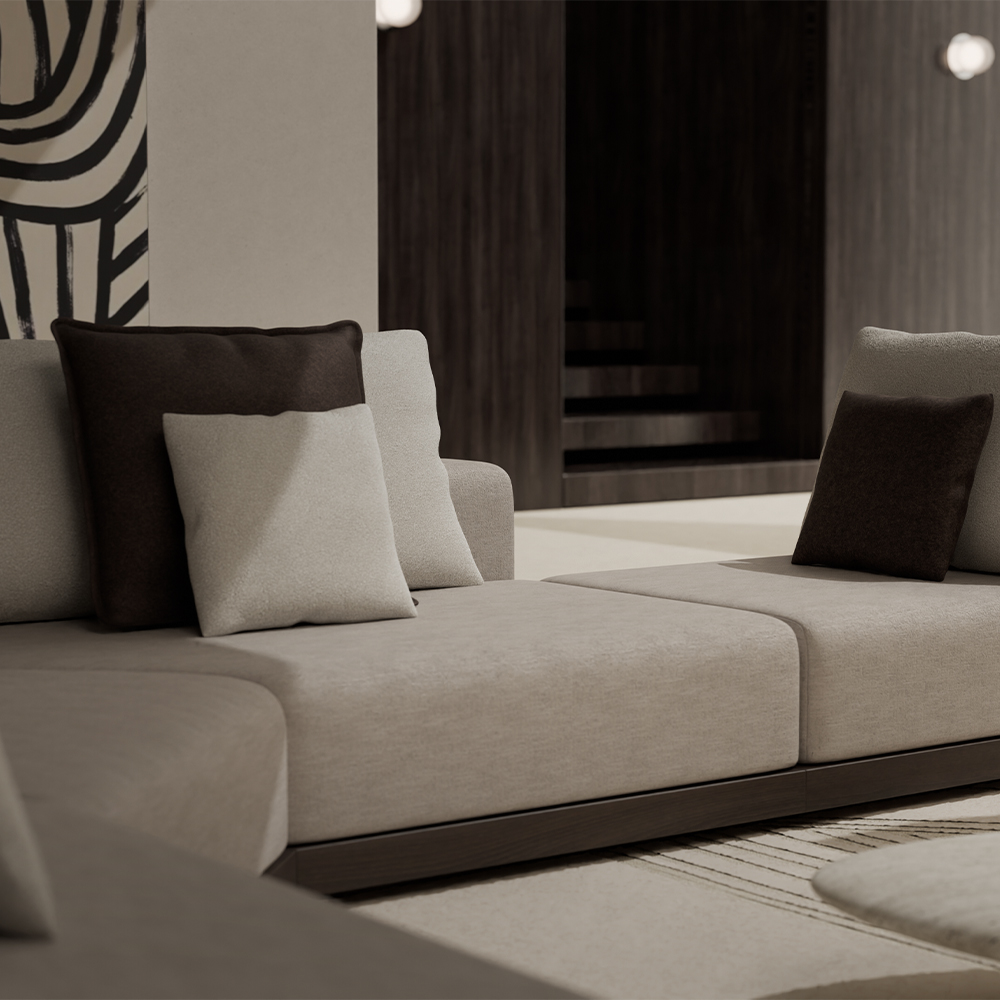 A modern beige sectional sofa with dark and light throw pillows graces this stylish living room. The space showcases neutral tones, abstract wall art, a glimpse of a staircase, and the understated elegance reminiscent of 11 Ravens design.