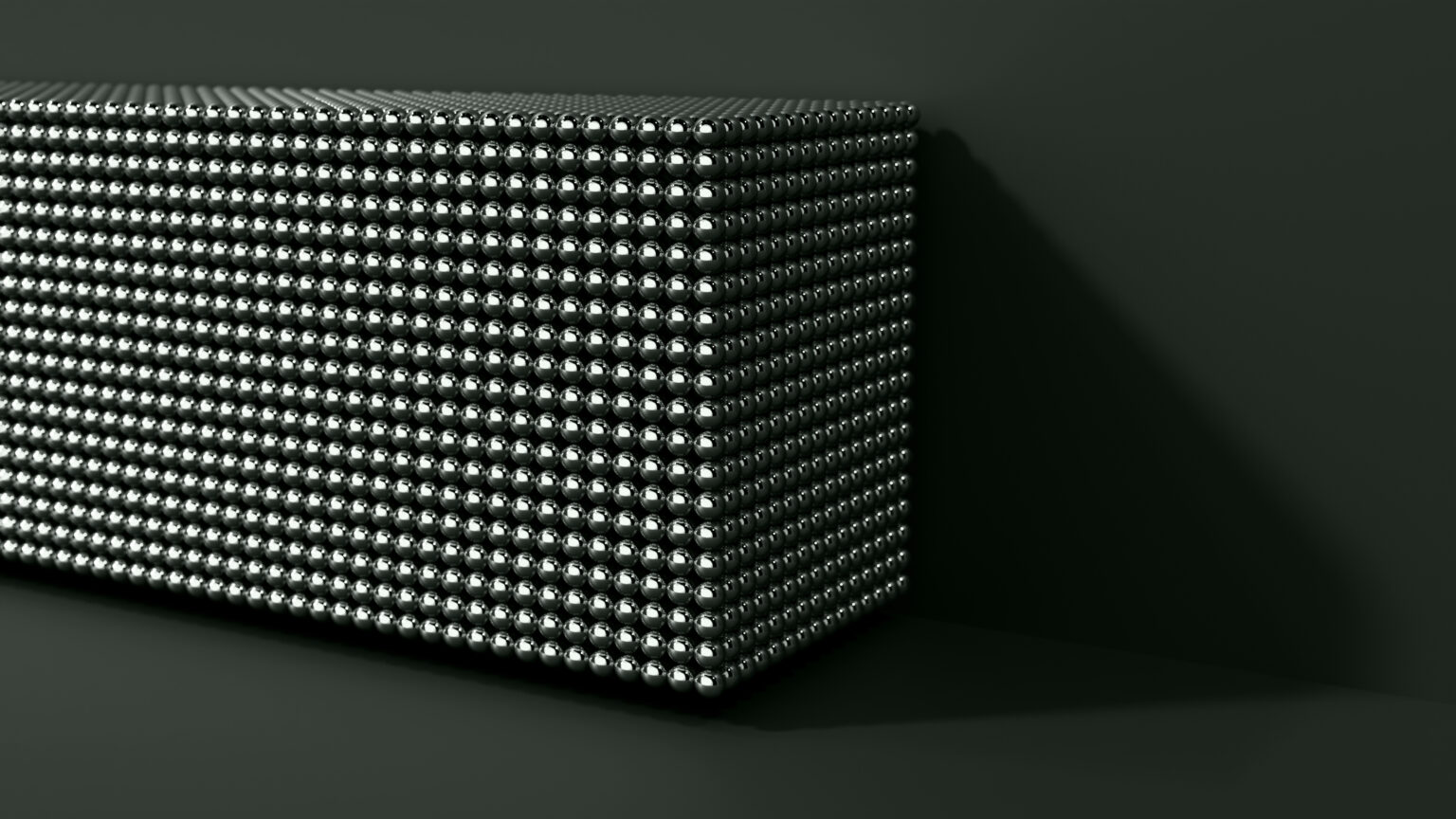 A rectangular block covered with a uniform grid of shiny metallic spheres, set against a dark background and casting a shadow to the right.