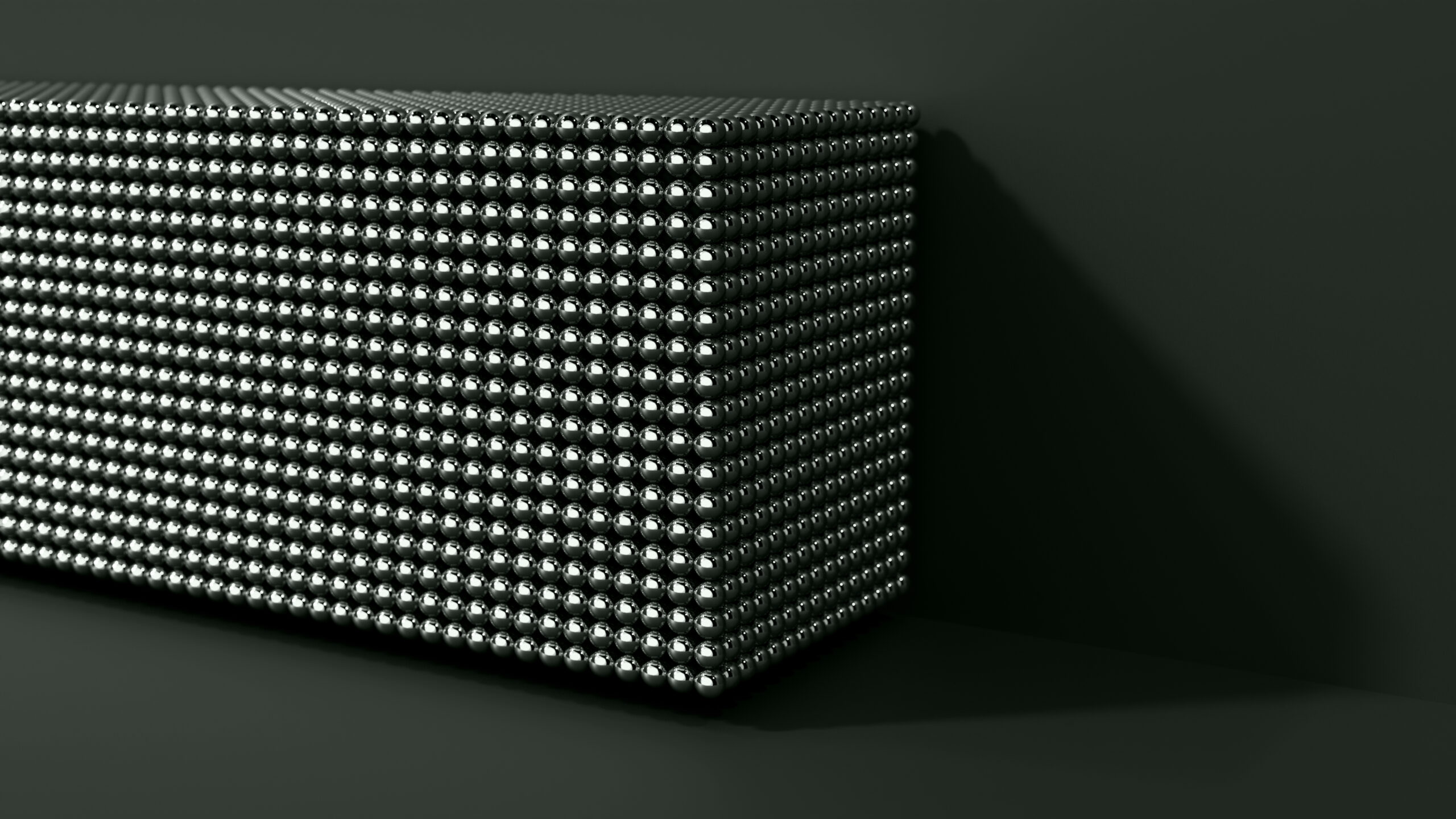 A rectangular block covered with a uniform grid of shiny metallic spheres, set against a dark background and casting a shadow to the right.