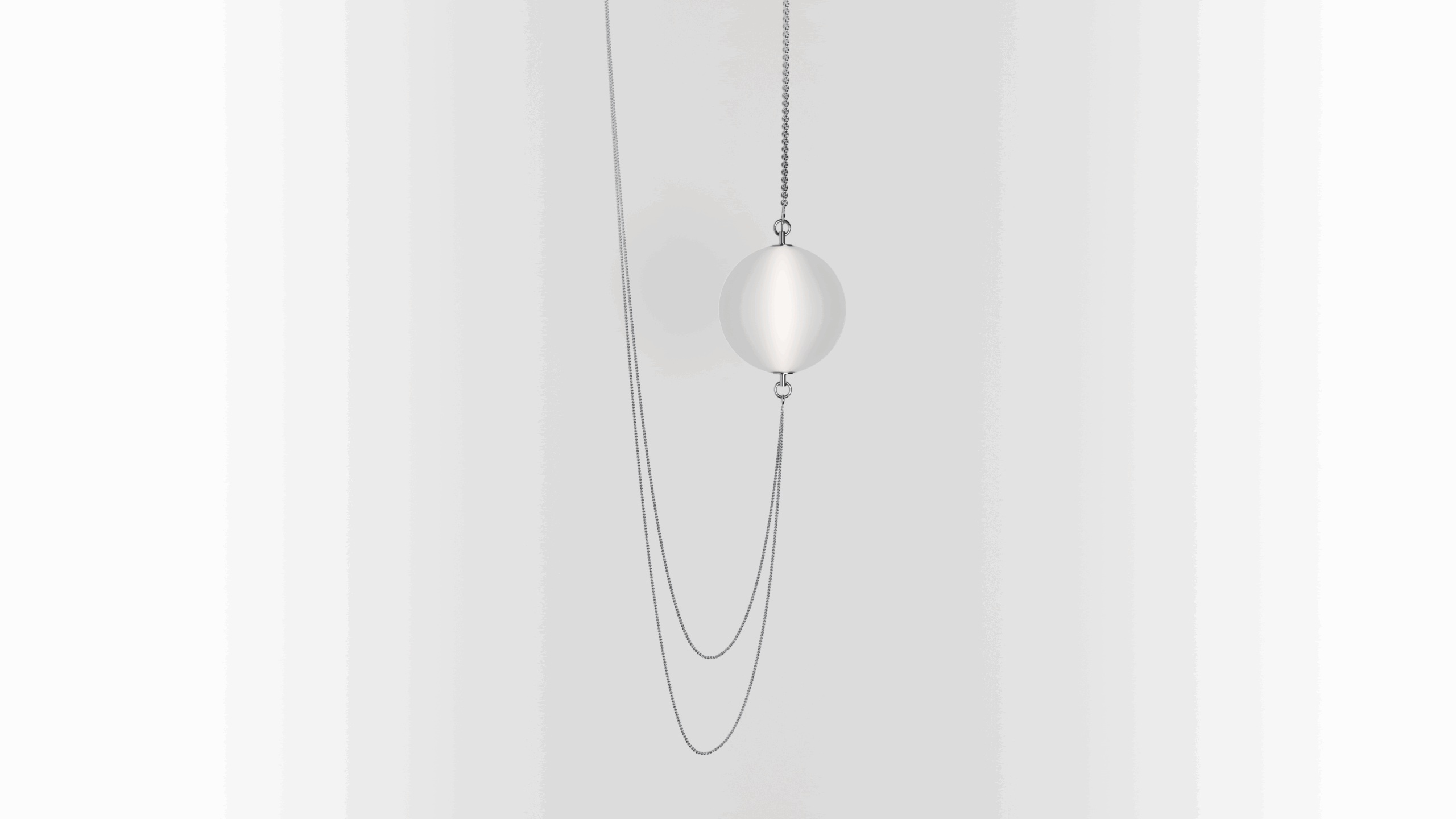 A silver necklace with a thin chain and a large, smooth, spherical pendant is suspended against a plain white background. The necklace forms a loose loop below the pendant.