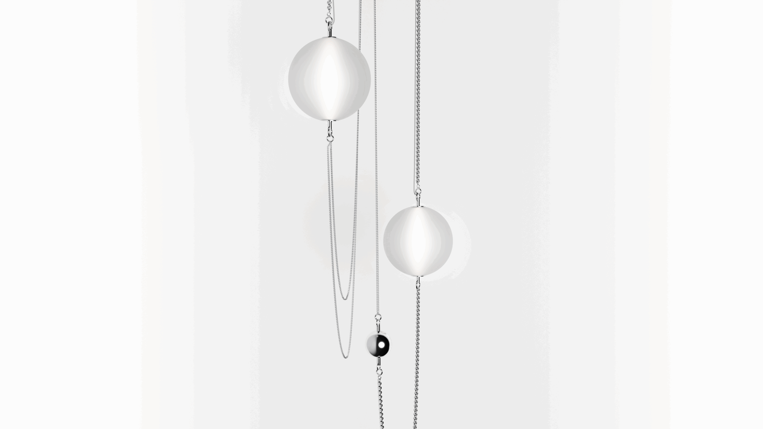 Minimalist image with three silver spheres and an oval black bead suspended on fine silver chains, hanging vertically against a plain white background. The arrangement is simple and modern.