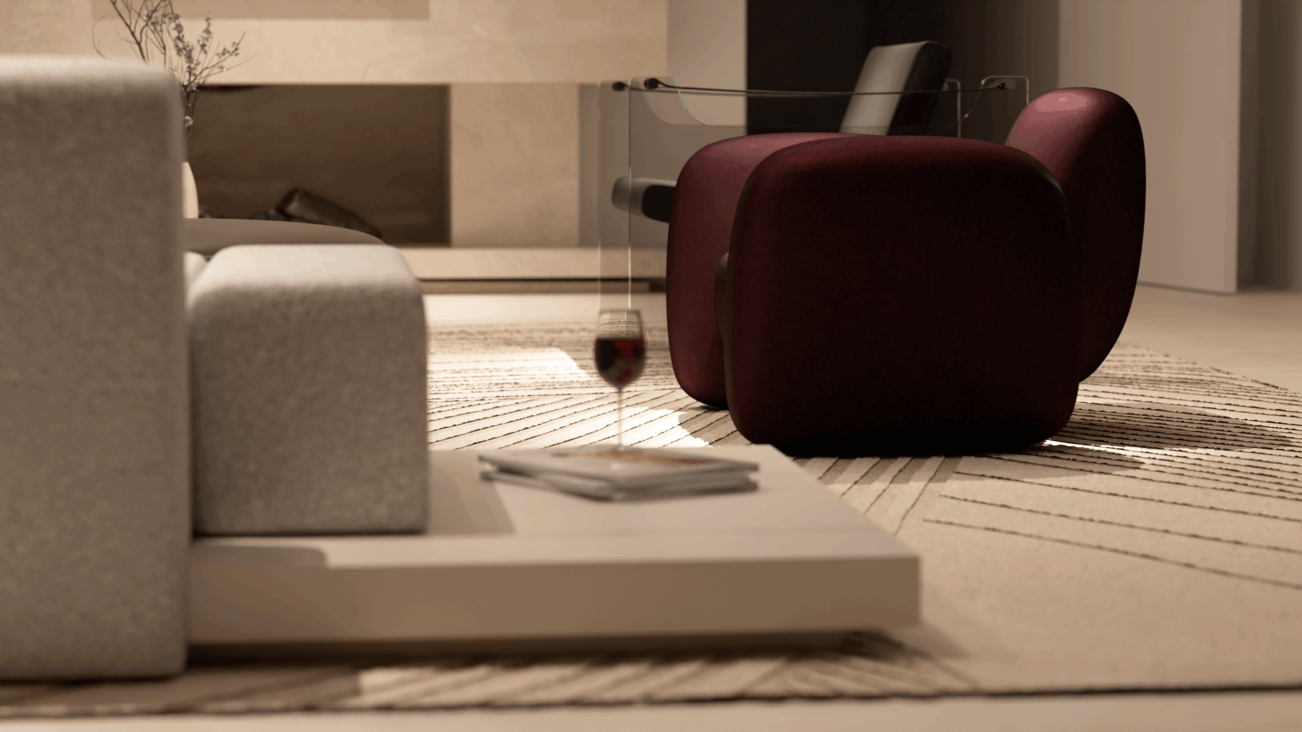 A modern living room with a light gray sofa, a burgundy armchair, a geometric-patterned rug, a coffee table holding a wine glass and a magazine, and soft, ambient lighting.
