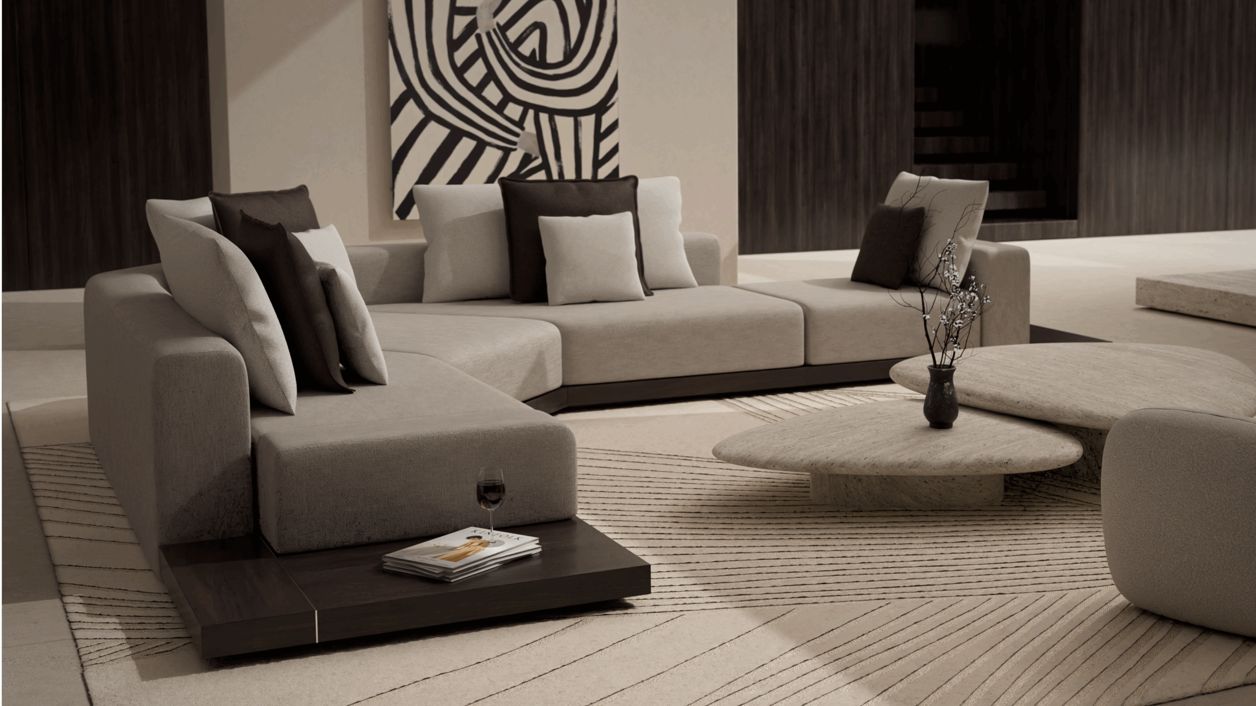 A modern living room with beige sectional sofas, brown and cream pillows, a low round coffee table, a glass of wine on a side table, and abstract black-and-white art on the wall. Neutral tones and minimalist decor.