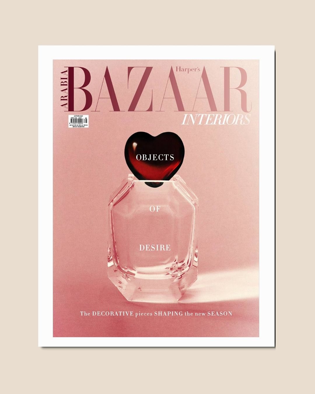 A Harper’s Bazaar Interiors Arabia magazine cover featuring a clear perfume bottle with a black heart-shaped cap against a soft pink background. The words Objects of Desire are written on the bottle.