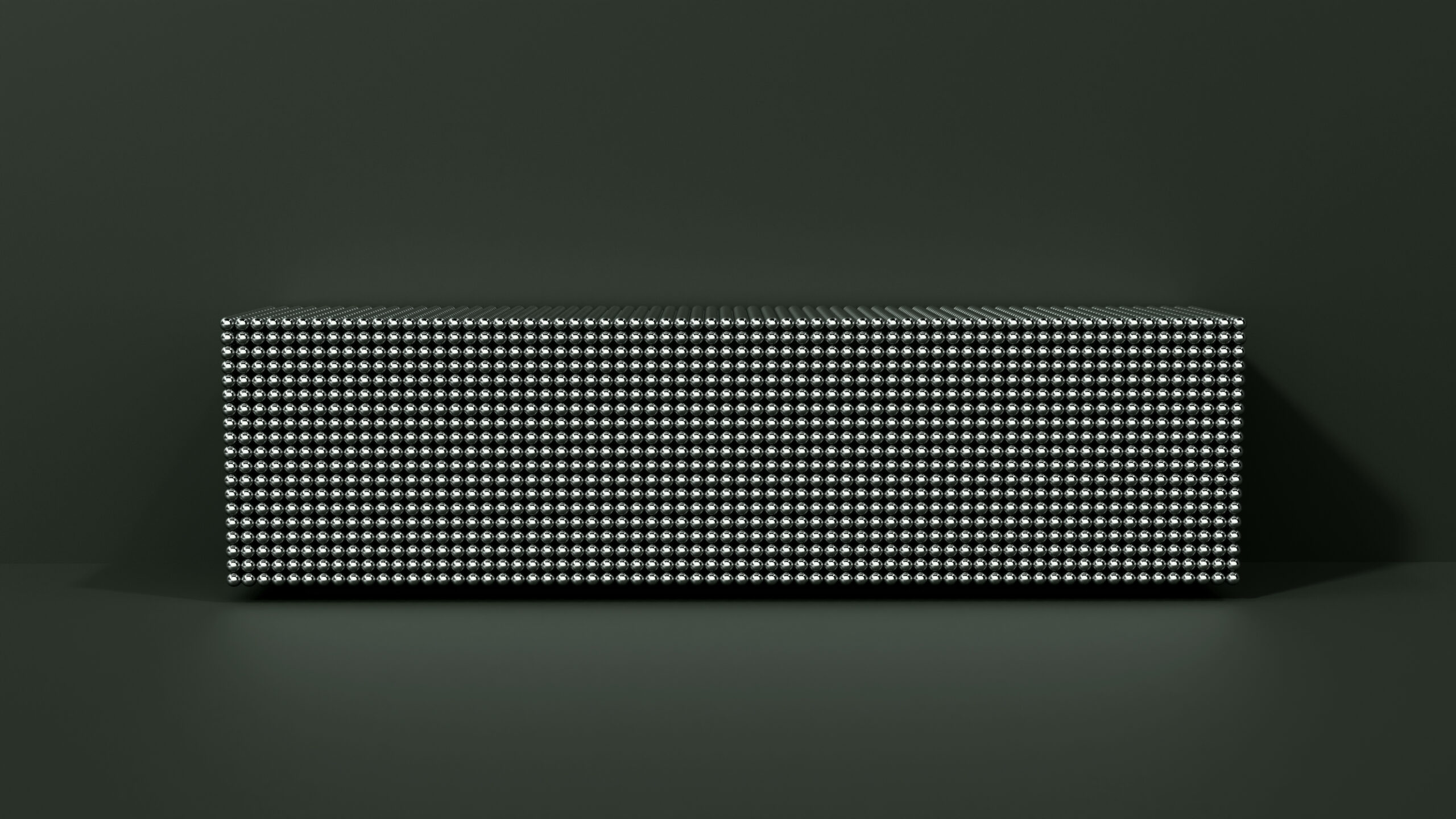 A rectangular box covered with a grid of small, evenly spaced white dots sits against a dark, matte background with soft lighting creating subtle shadows.