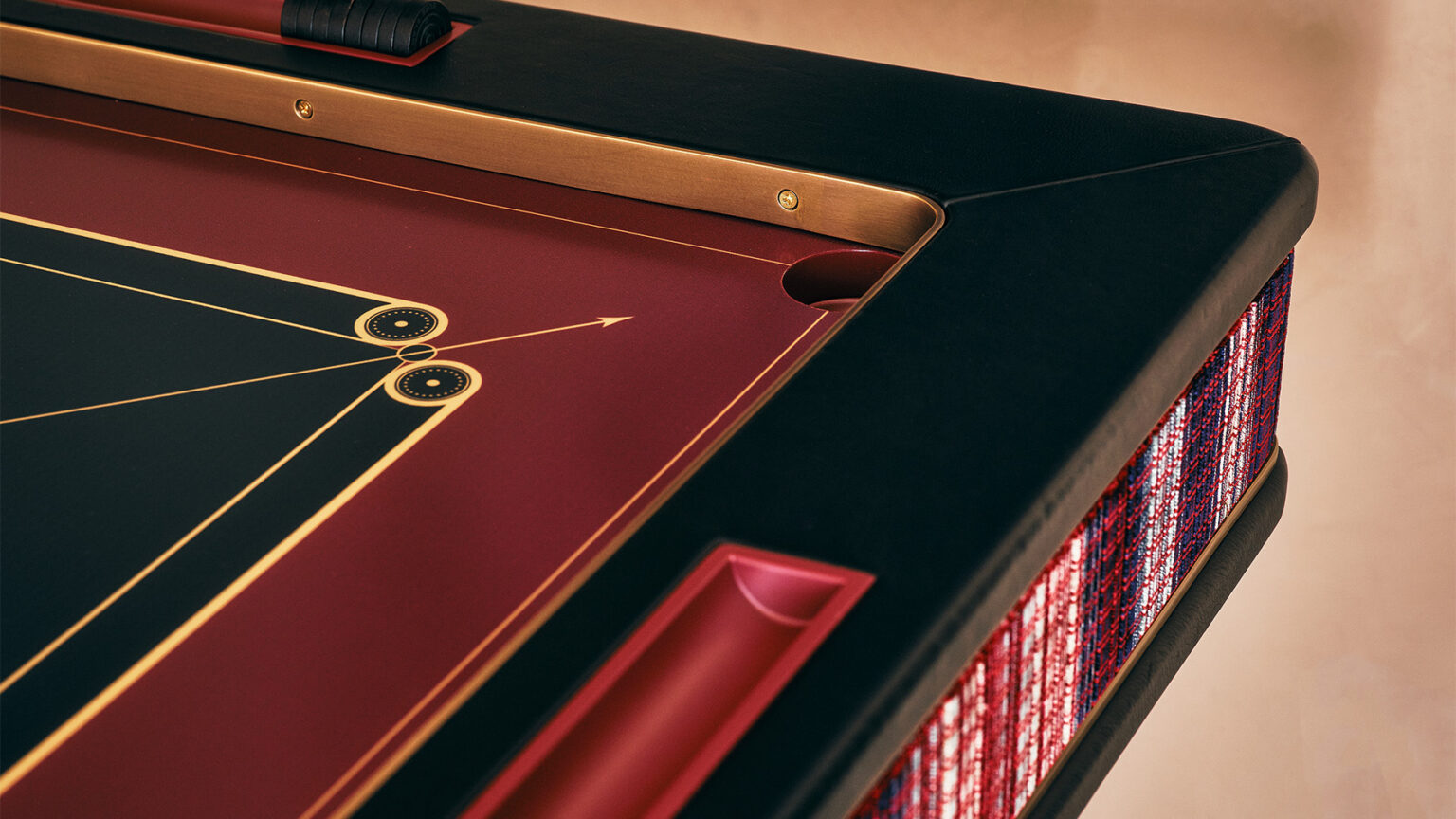 Close-up of a luxury handcrafted pool table with a red and black surface, gold accents, and sleek black rail. The table features geometric designs and woven multicolored side panels—a striking addition to upscale game tables.