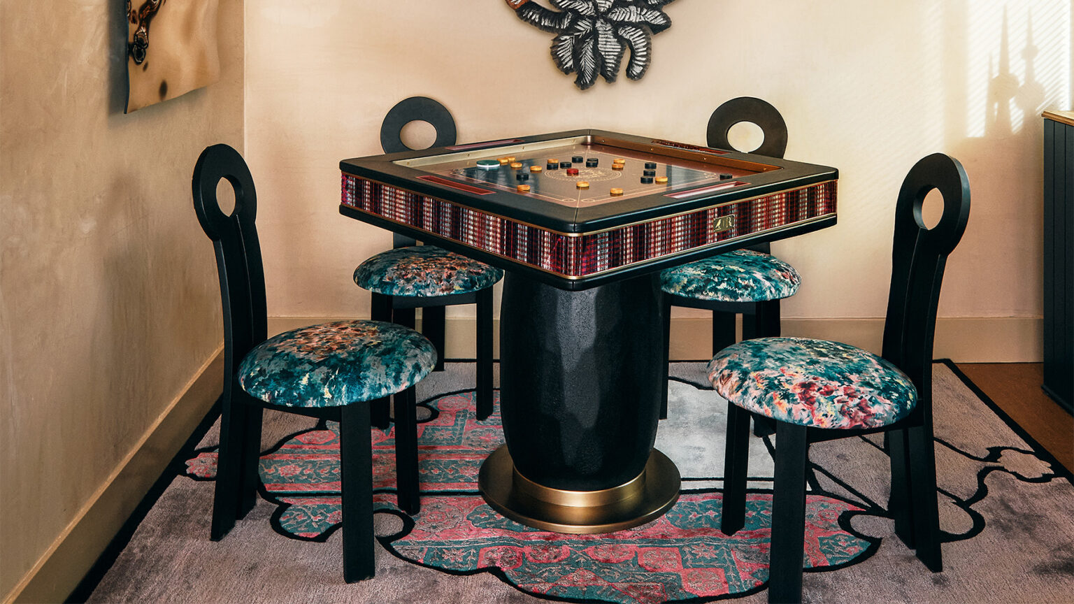 A handcrafted square game table with colorful pieces is surrounded by four black chairs with circular backrests and patterned cushioned seats, sitting on a decorative rug in a cozy corner, creating a touch of luxury.
